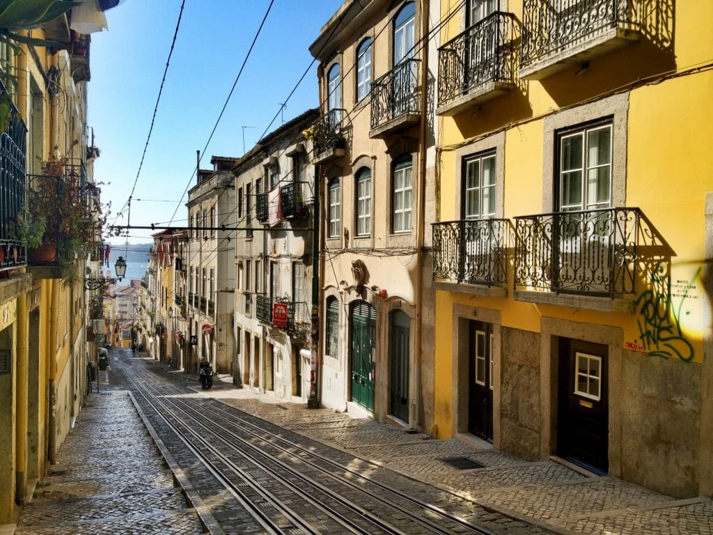 A steep street with yellow buildings on each side of it.