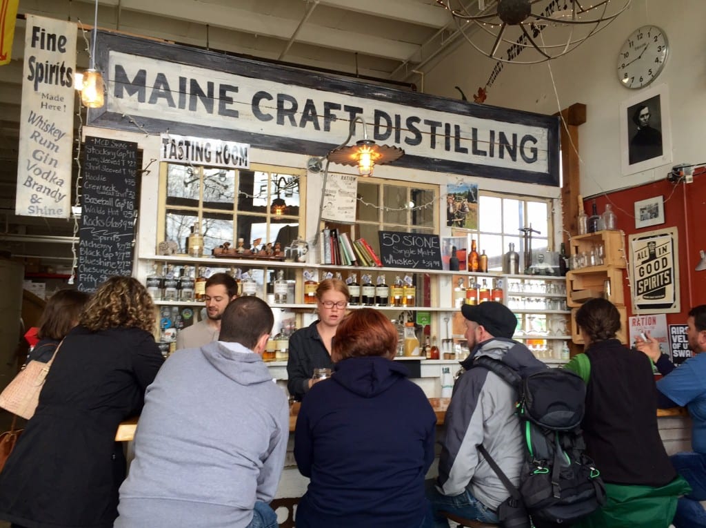 A group of people in hoodies sitting at a bar with a big sign reading "Maine Craft Distilling"