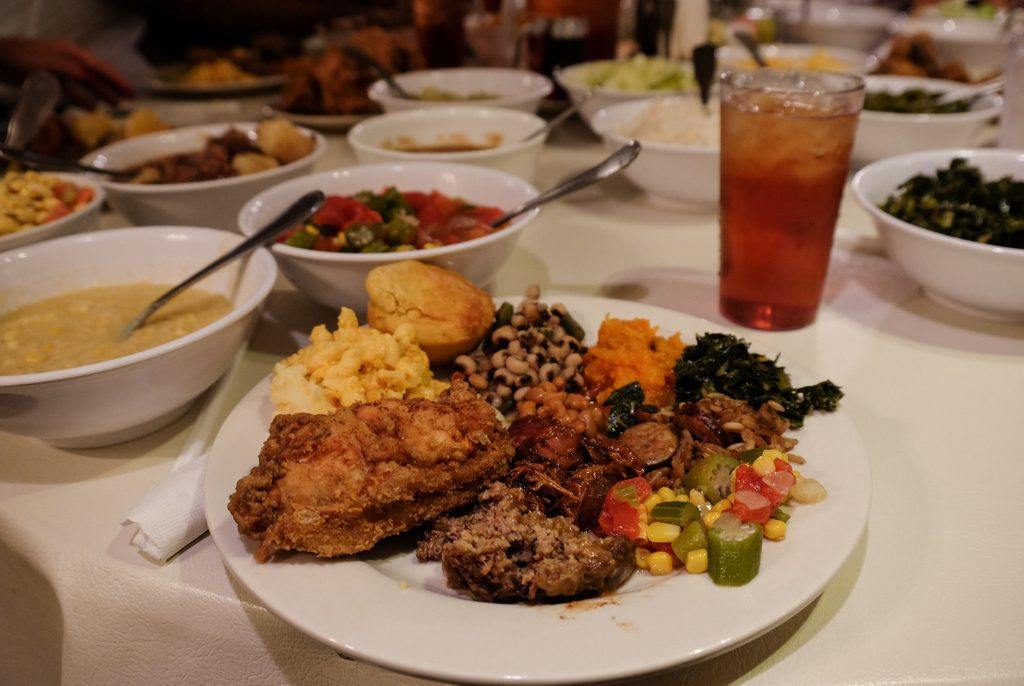 A plateful of food -- fried chicken, cornbread, black eyed peas, squash, and more -- with family-style plates in the background at Mrs. Wilkes' Dining Room in Savannah.