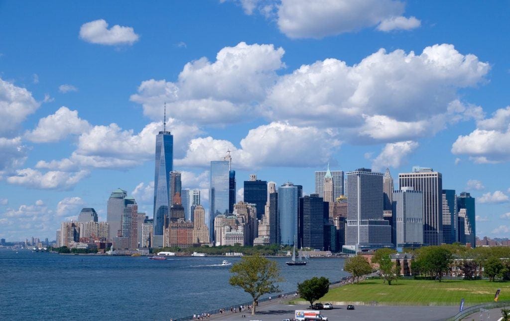 The Manhattan skyline underneath a partly cloudy sky, buildings rising up in shades of blue and gray.