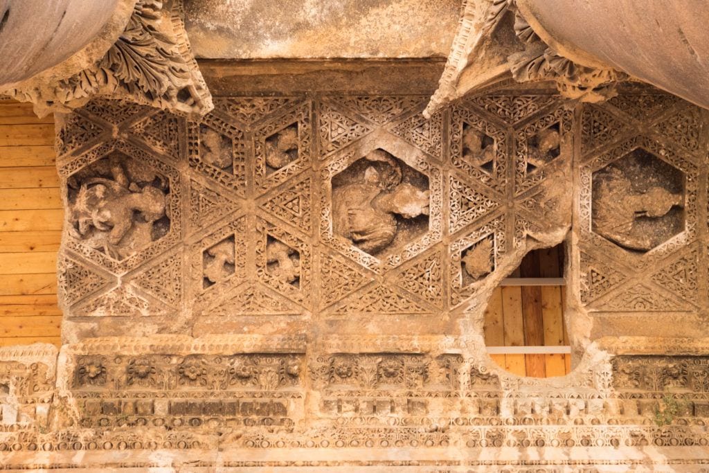 The ceiling of one of the temples in Baalbek: an intricate carved pattern in the sandstone, some parts eroded away, some of the missing parts replaced with wooden boards.