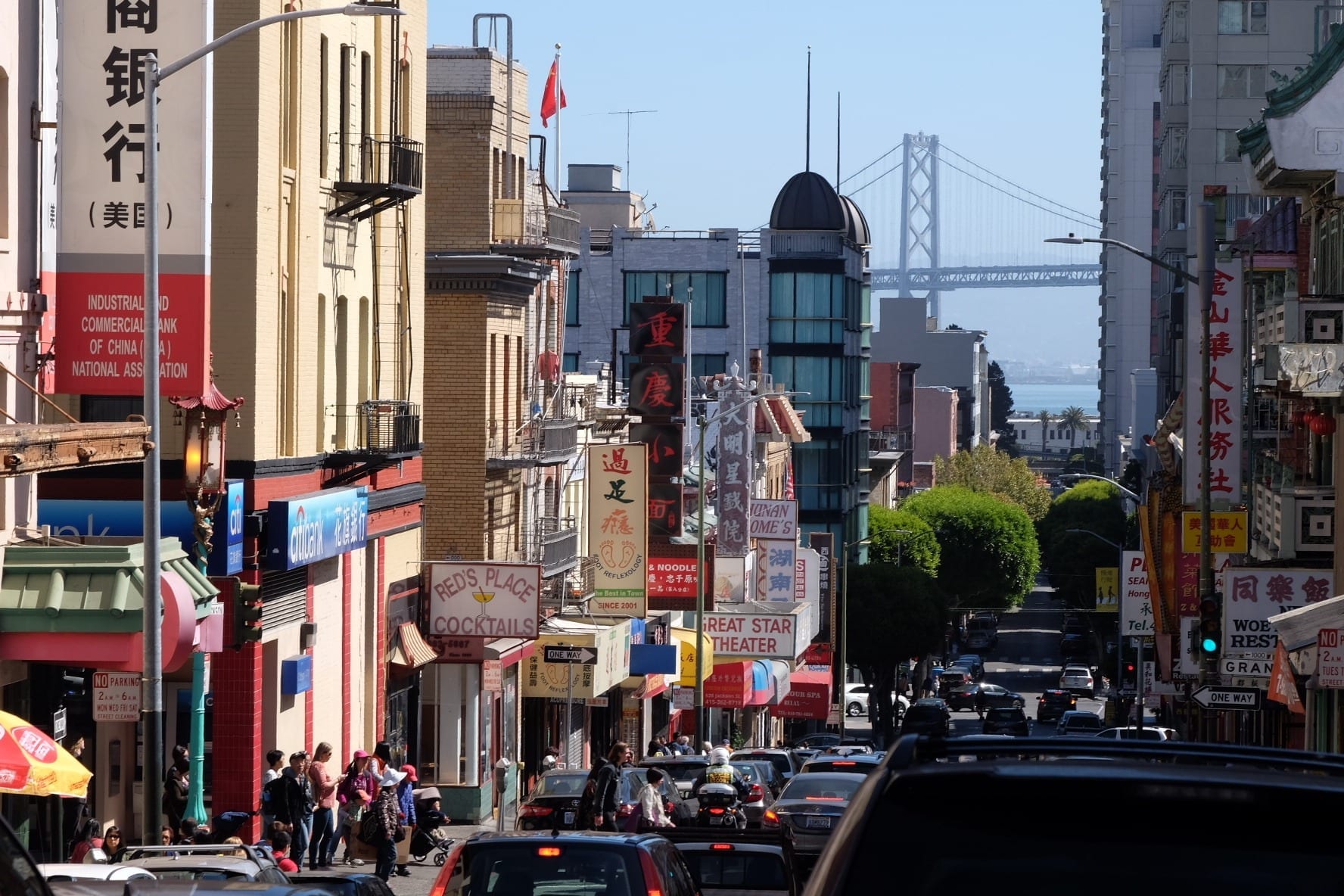 View over Chinatown in San Francisco, lots of store signs jutting out at angles, leading to a bridge underneath a blue sky.