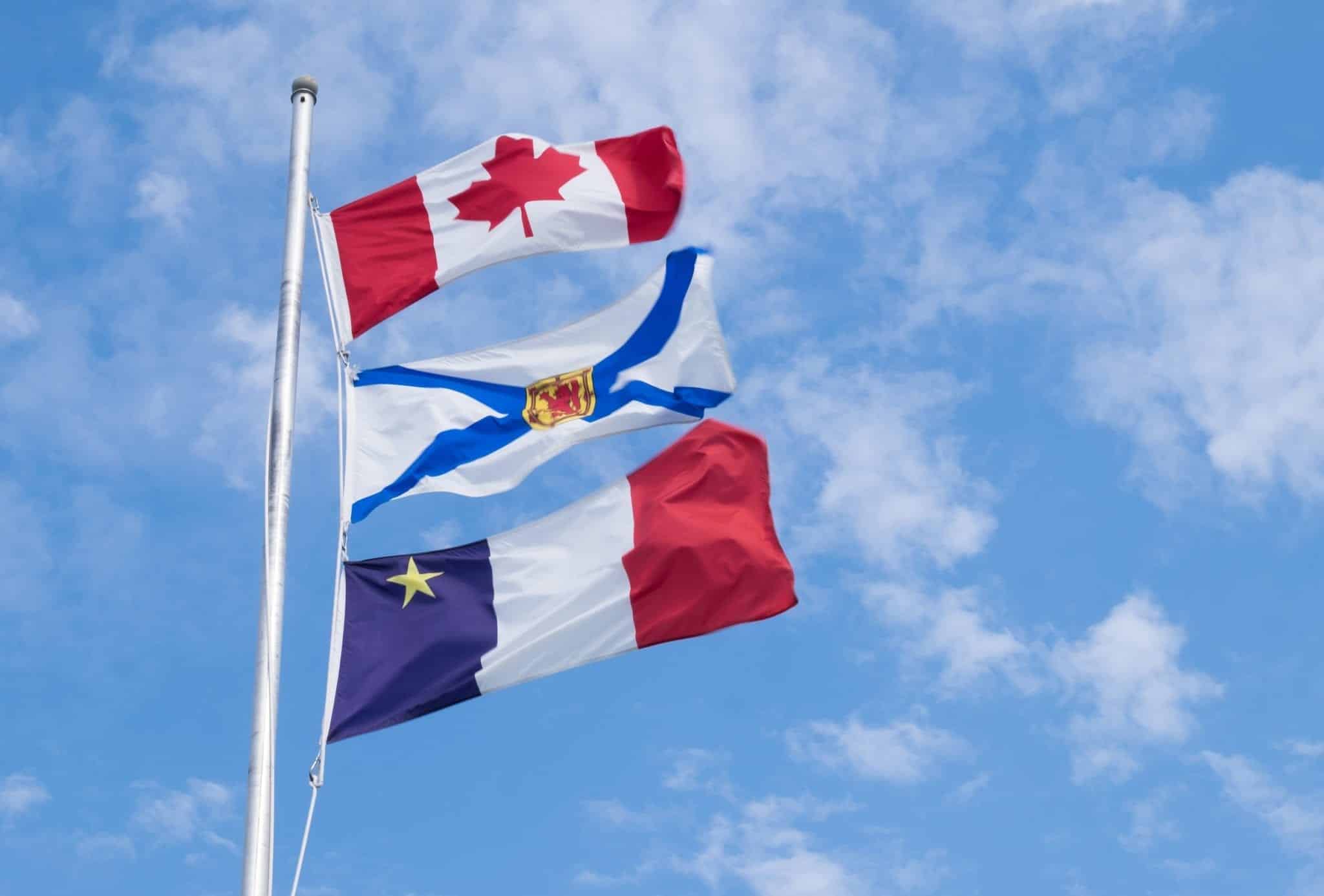 The Canadian, Nova Scotian, and Acadian flags set against a blue sky.