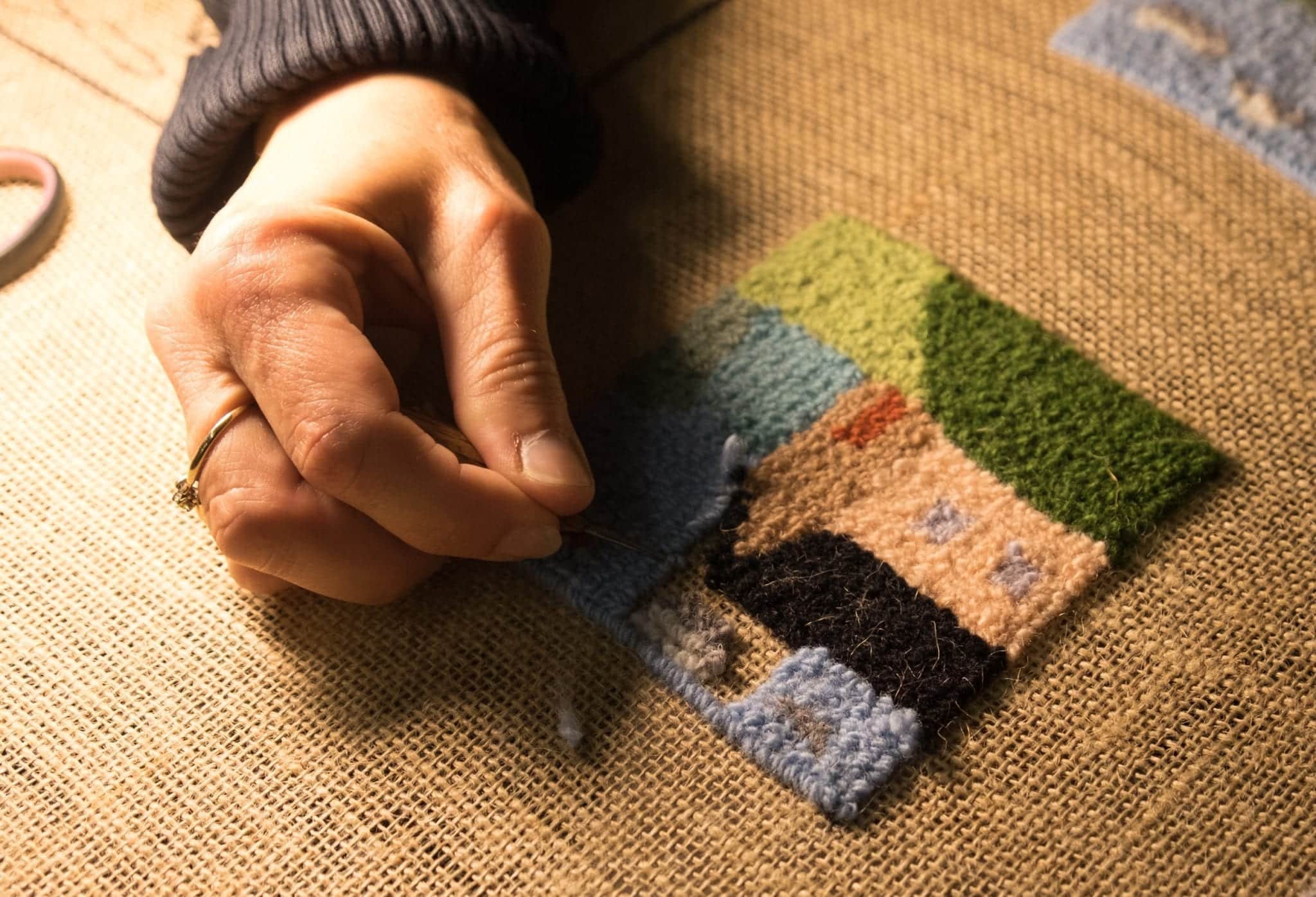 A woman's hand hooks wool through the backing to make a rug.