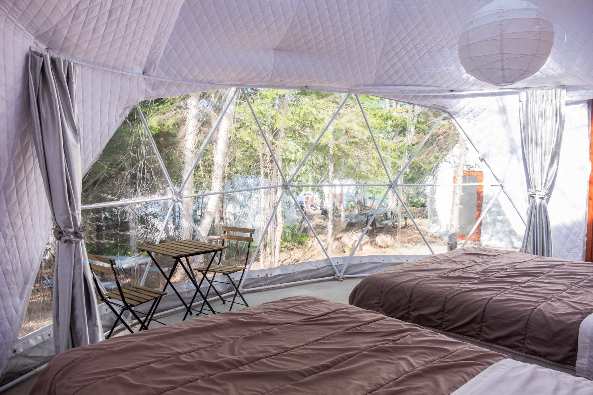Two beds side by side in front of the triangular windows of the Blue Bayou Geodesic Domes