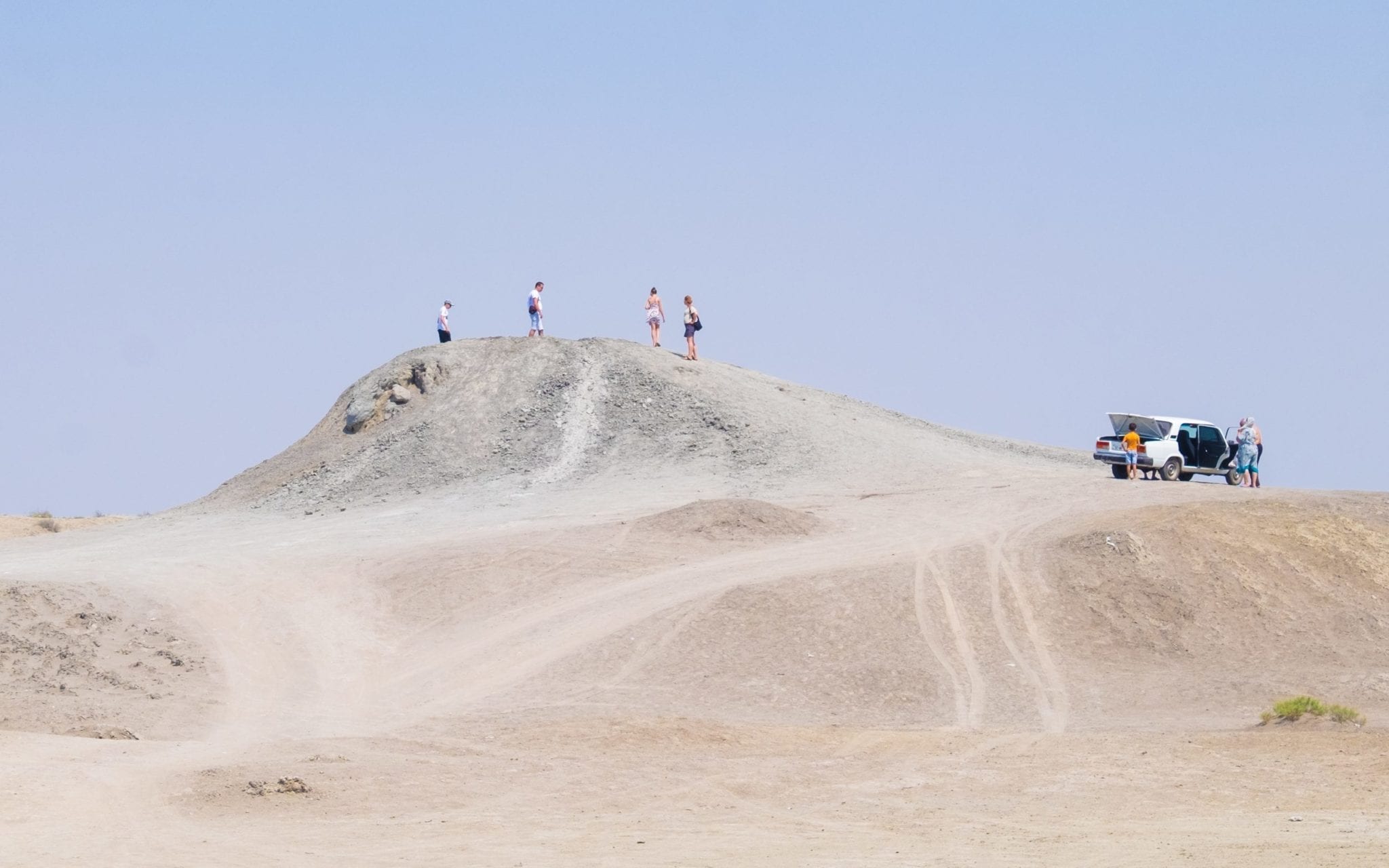 Four tiny people standing atop a mud volcano in the desert, making it look enormous.