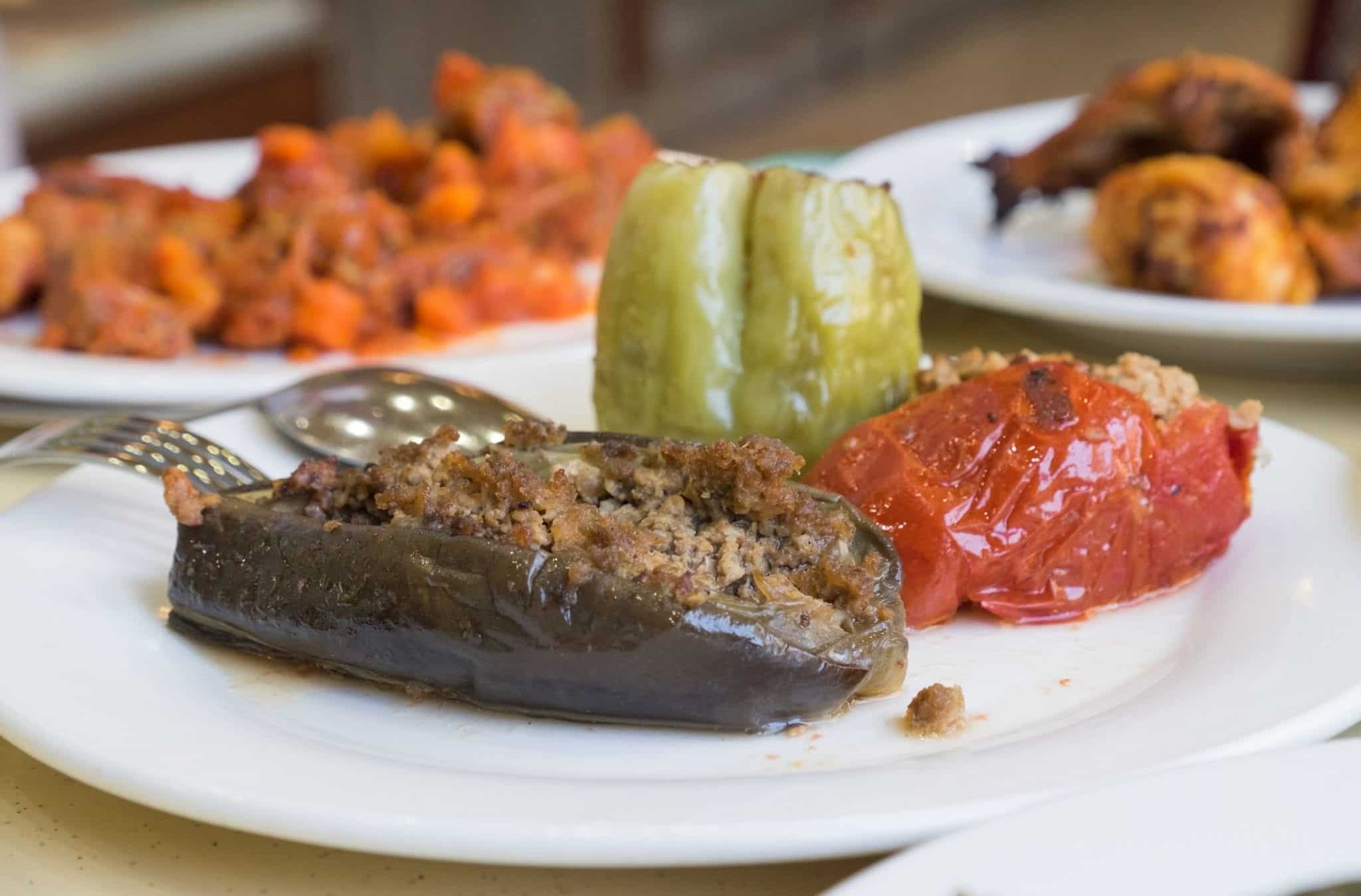 On a plate, an eggplant and two kinds of peppers stuffed with minced beef.