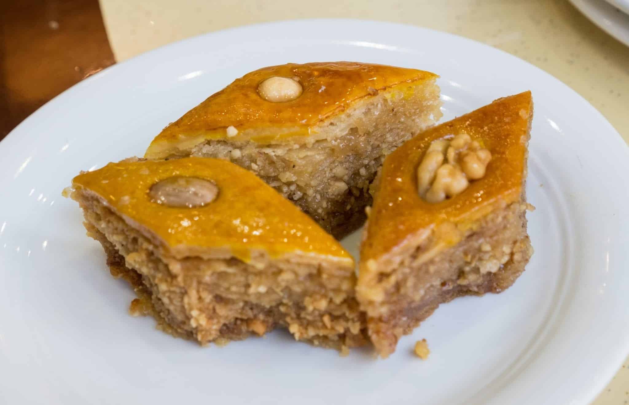 Three pieces of baklava, one topped with an almond, one with a walnut, one with a hazelnut.