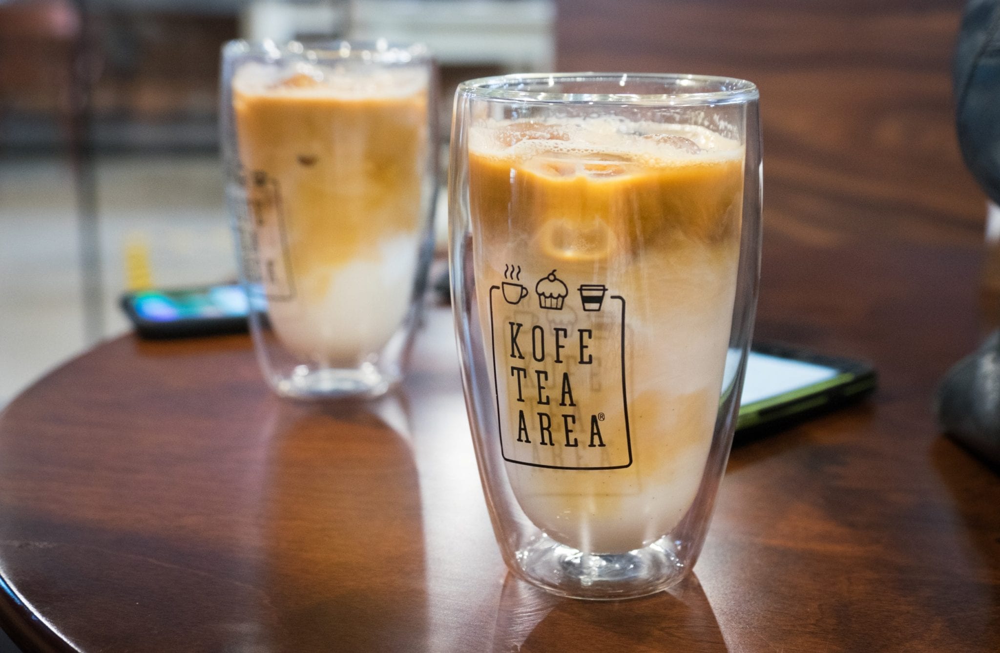 Two clear plastic large lattes with the milk and coffee swirling together, surrounded by ice.
