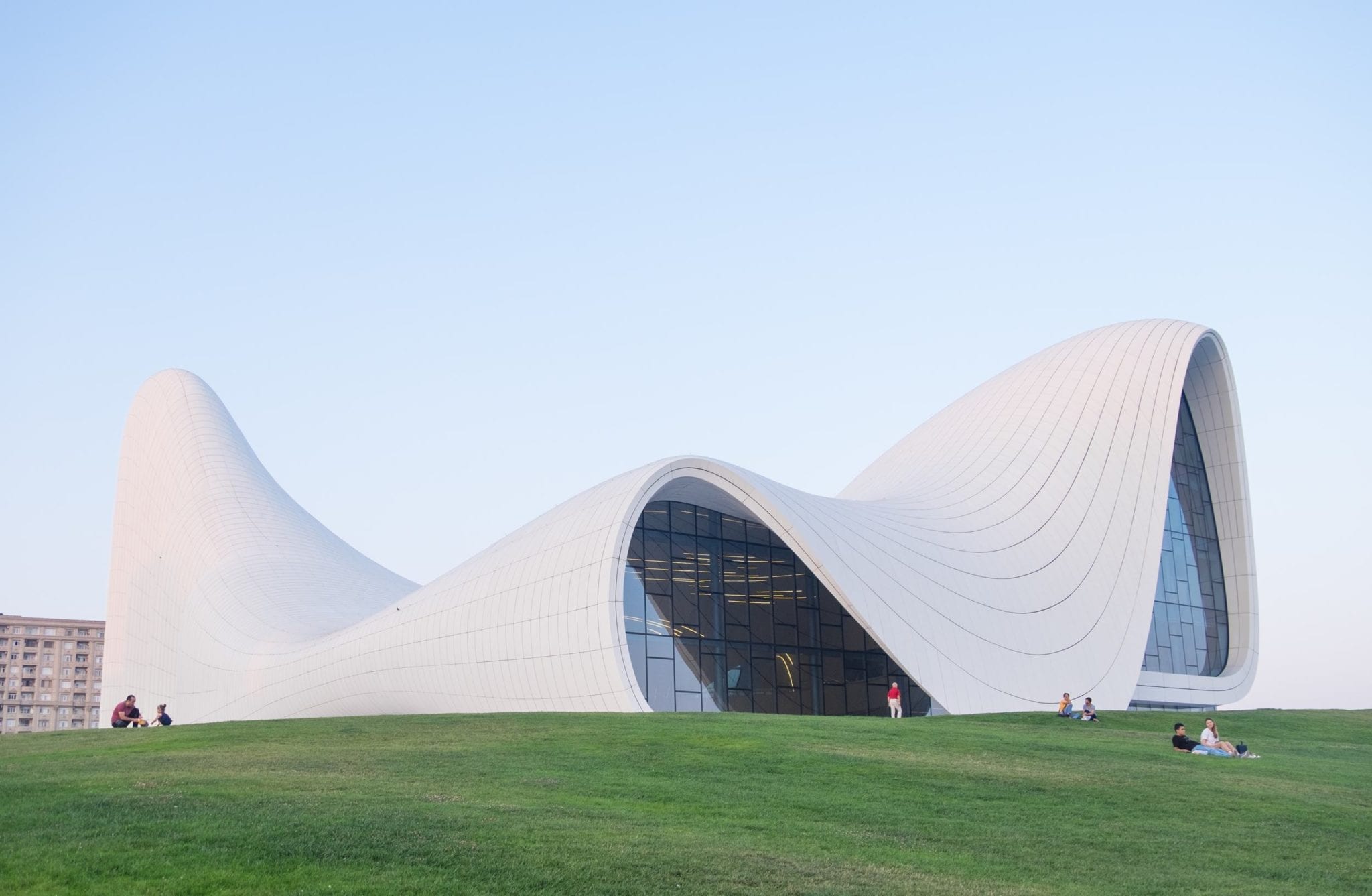 The swooping white curves of the modern Heydar Alivev Center, with people sitting on the grass in front of it.
