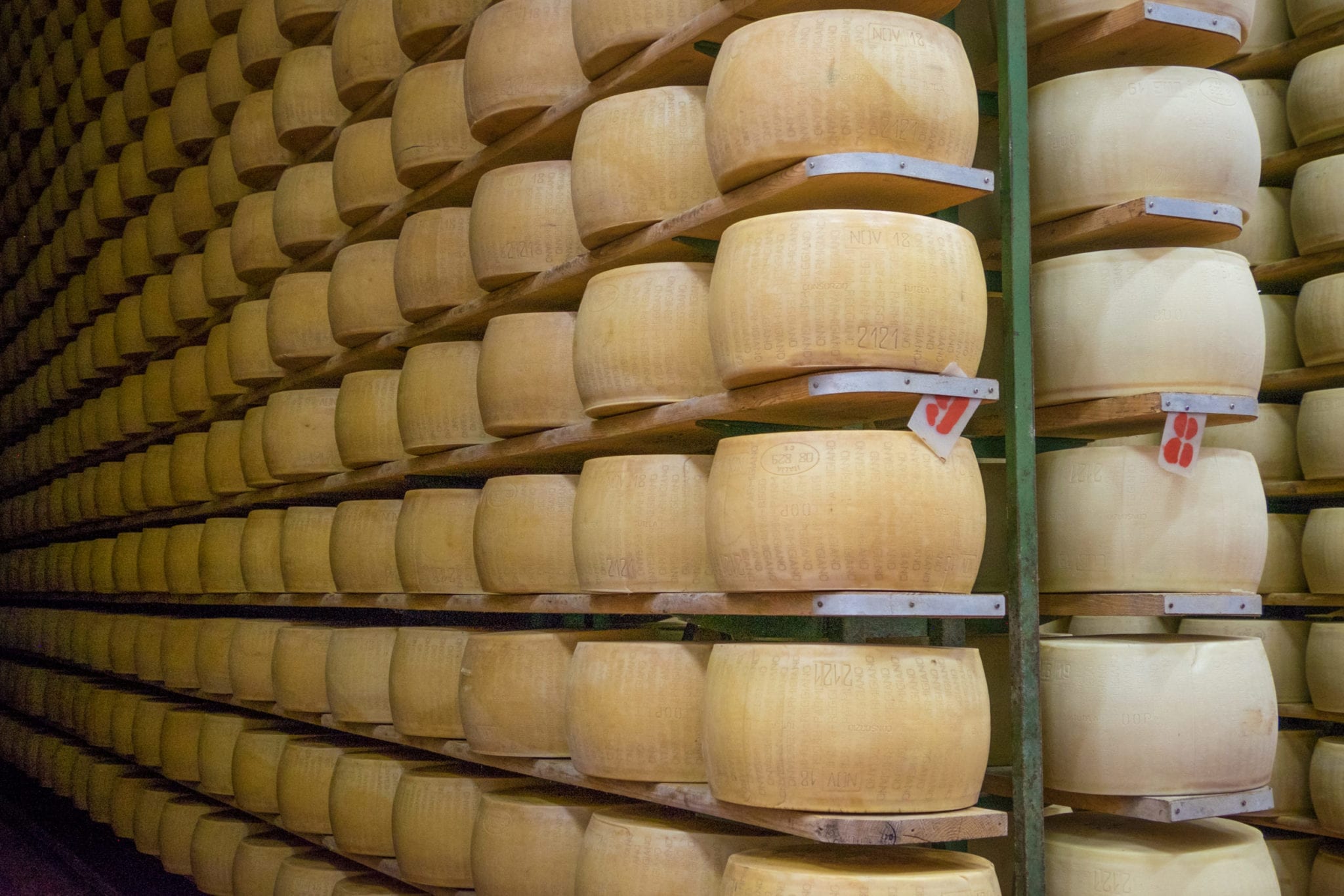 Rows and stacks of Parmigiano Reggiano wheels on shelves.