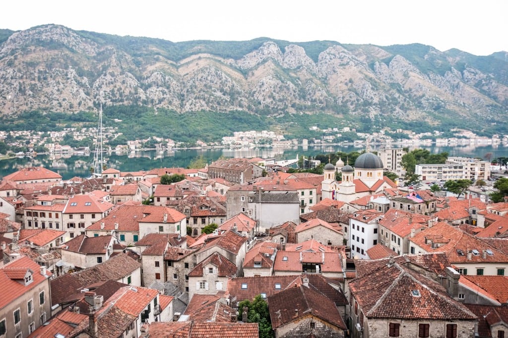 Orange roofs of Kotor against a gray-green mountain backdrop at dawn.