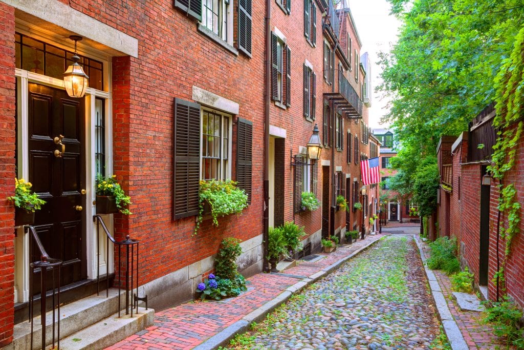 A small cobblestone street in the Beacon Hill neighborhood, edged with historic red brick buildings.