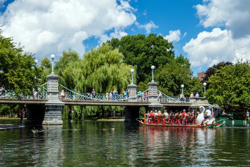 One of Boston's swan boats -- a wooden boat topped with rows of benches, in the back is a wooden swan behind which a driver sits -- about to go underneath a small suspension bridge (the smallest in the world, actually). 