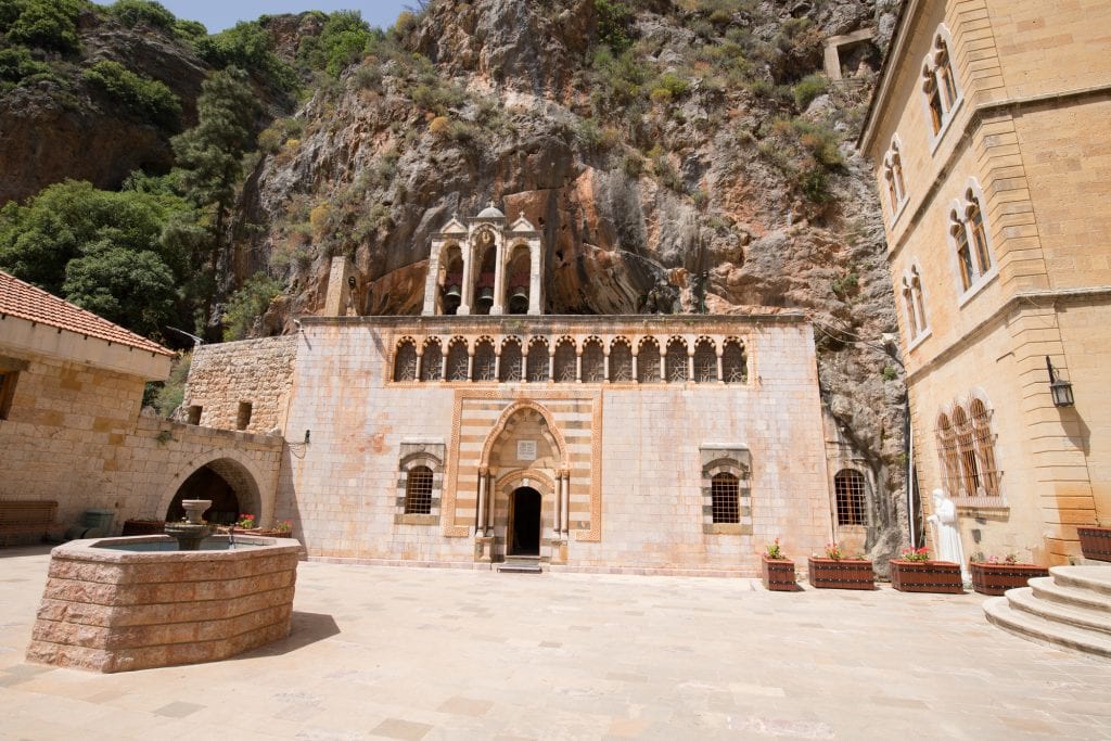 In front of a big wall of stone, you see sand-colored church, with windows and arched doorways carved out of it. It looks like it's growing from the stone.