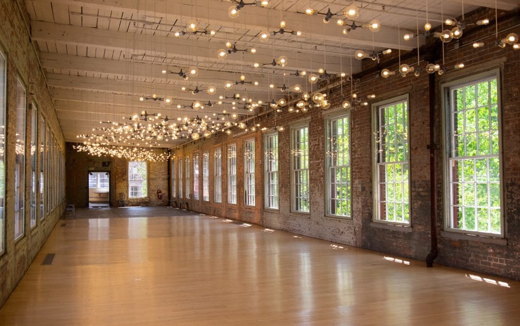 A long room at Mass MoCA -- it's long, red brick, covered with super huge windows letting in lots of light, and dozens of modern orb lights dangling from the white wooden ceiling.