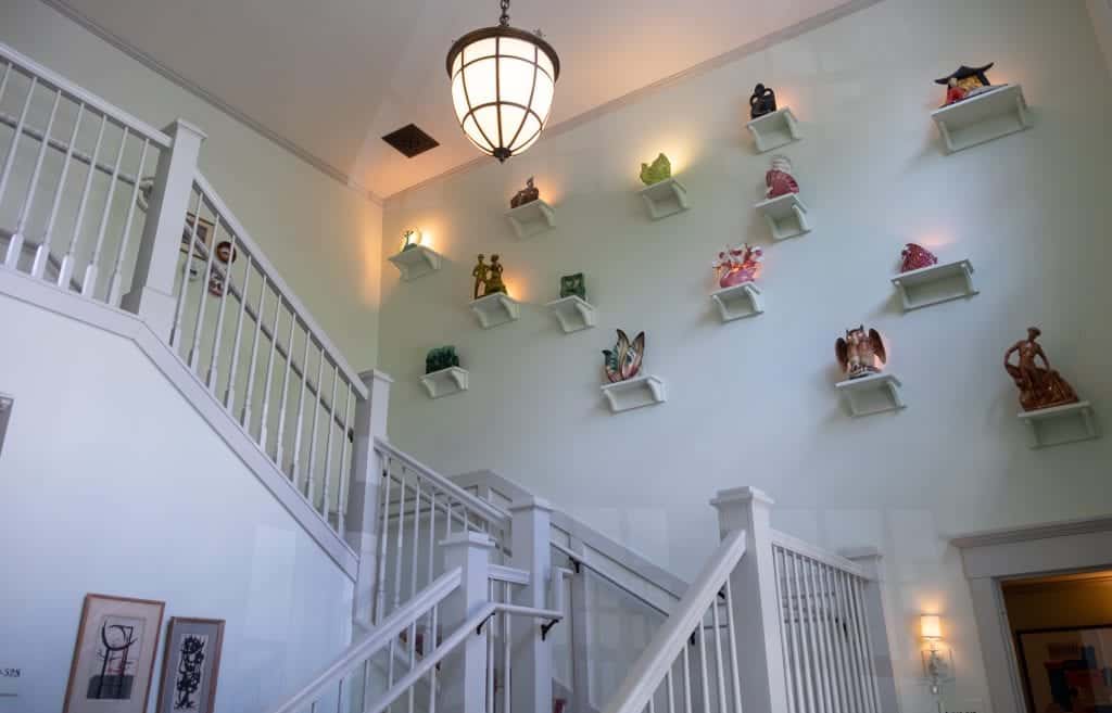 The hallway at the hotel: a white staircase and on a wall, several small shelves attached to the wall, each topped with a small glass sculpture.