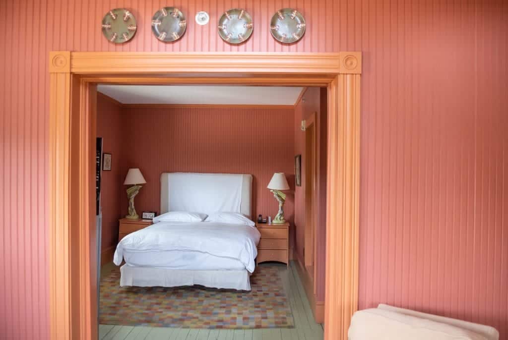 A room with textured stripe walls -- the walls are dark reddish orange and the trim is brighter orange, like the color of goldfish crackers. You see a white bed in the background in between two end tables with lamps that look like the sculpture of a man in green gauze.