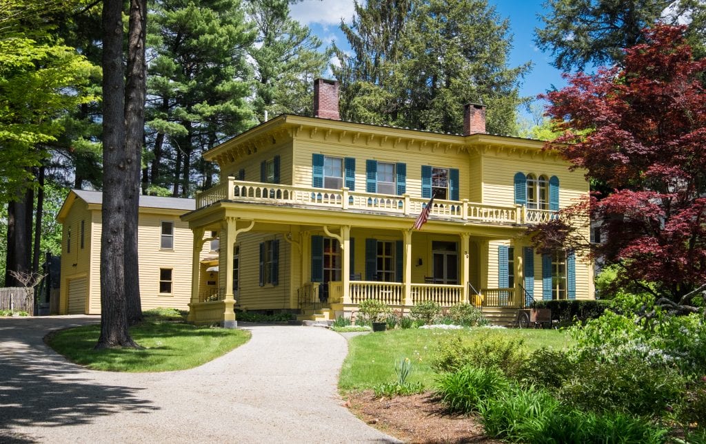 An old-fashioned yellow house that looks like it has a widow's walk (a porch above the first story you can walk on). It's nestled into the trees like a storybook.