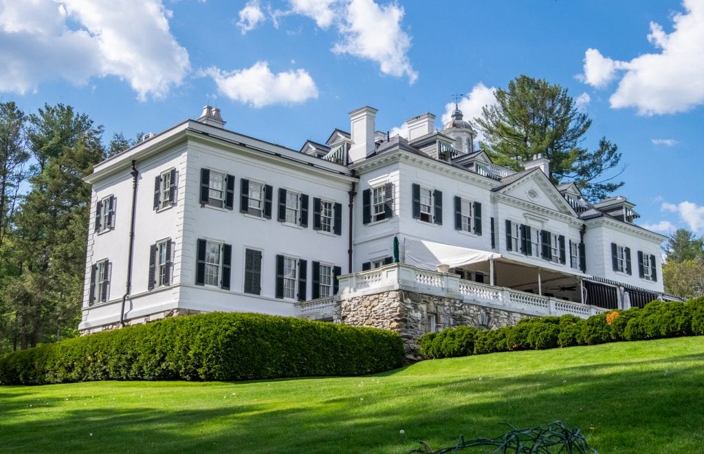 A huge white mansion with lots of black shutters on a hill in the Berkshires.