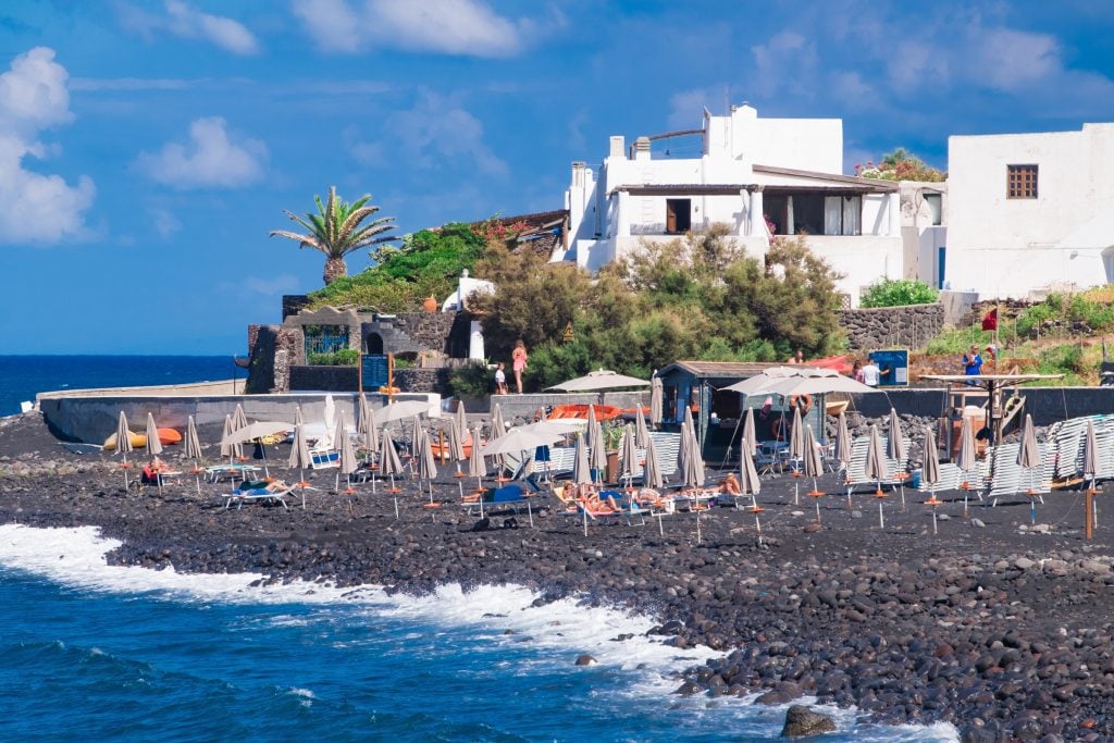 A gray rocky beach topped with umbrellas and chairs next to them on Ficogrande on Stromboli.