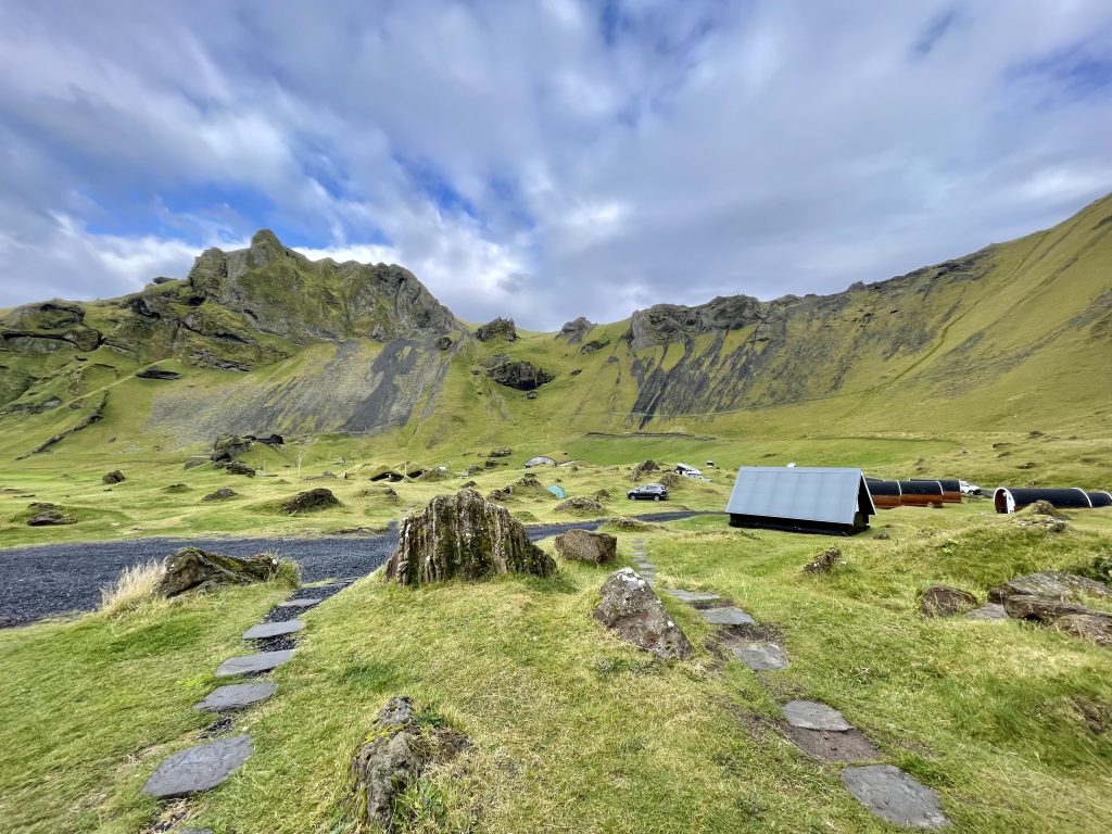 A mountainous green landscape topped with tiny cabins and tents.