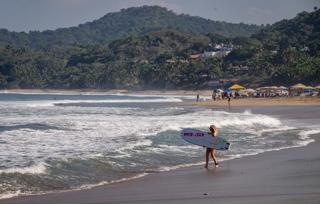 A woman holding a surfboard and walking into the ocean.