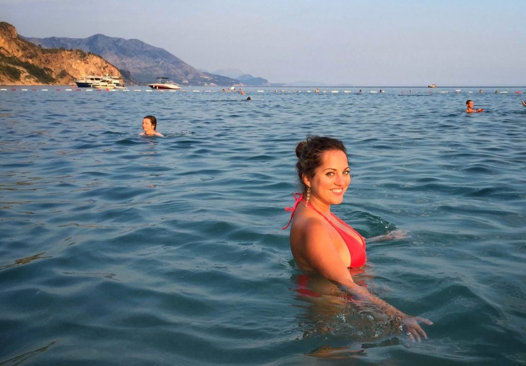 Kate smiling big while swimming in the Adriatic, wearing a red bikini.