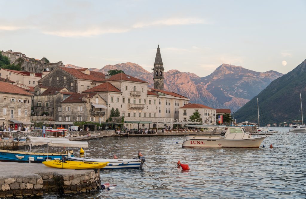 The calm fjord side town of Perast, with lots of ancient palaces on the edge of the water, and tall mountains rising up in the background.
