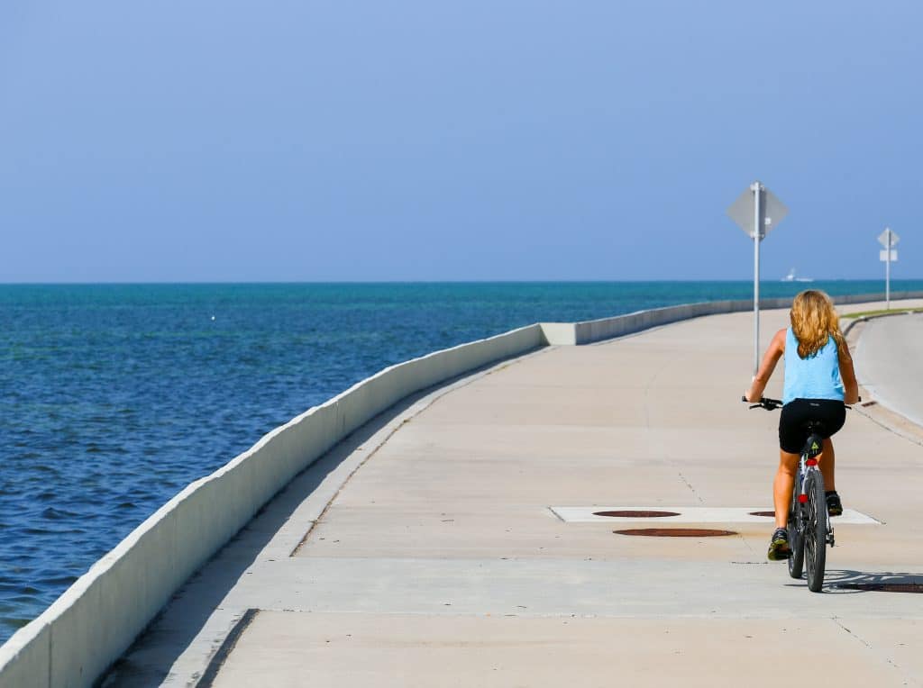 A woman biking on a cement road over the ocean.