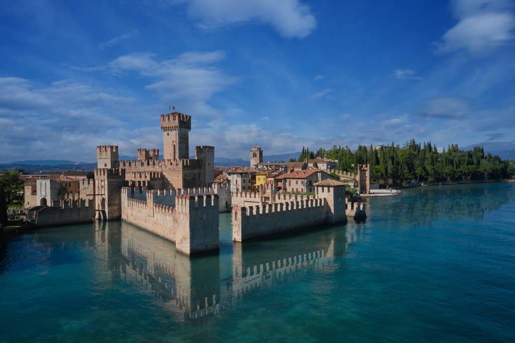 A gorgeous medieval castle perched on an island on a still blue-green lake.