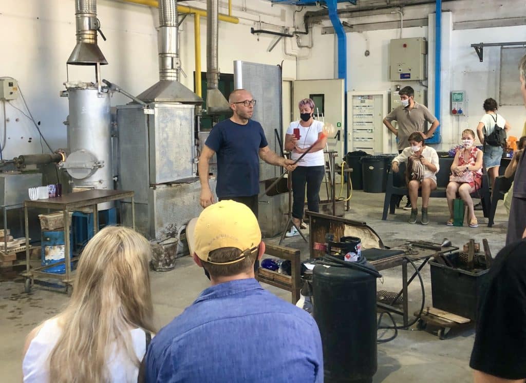 A glassblowing artist demonstrates how to shape glass to an audience.
